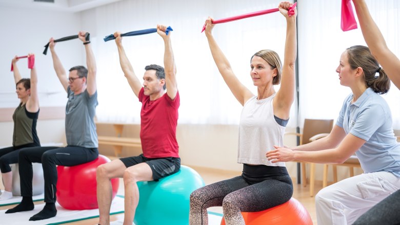 Heilgymnastik in der Gruppe, © Moorheilbad Harbach Gruppe von Menschen bei Gymnastikübungen auf Gymnastikbällen mit Therabändern.