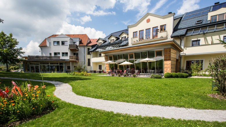 Hausansicht, © Gesundheitshotel Klosterberg GmbH Großes Haus mit Garten und Terrasse, umgeben von grüner Wiese und Blumen.