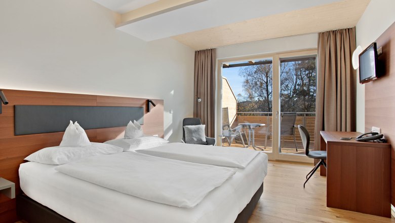 Zimmer, Kategorie A, © Gesundheitshotel Klosterberg GmbH Modernes Hotelzimmer mit Doppelbett, Schreibtisch, Fernseher und Balkon mit Blick ins Freie.