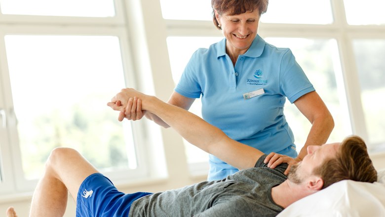Physiotherapie, © Doris Schwarz-König Eine Physiotherapeutin behandelt den Arm eines liegenden Mannes.
