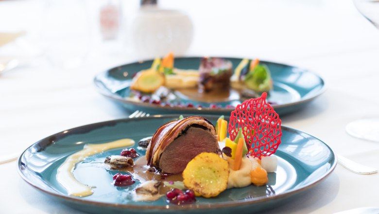 Kulinarik, © Gesundheitsresort Königsberg Gourmetgericht auf einem blauen Teller, kunstvoll angerichtet mit Fleisch, Gemüse und einer roten Dekoration.