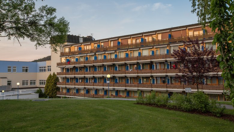 Das Kurhotel des Gesundheitsresort Königsberg, © Gesundheitsresort Königsberg Außenansicht des Kurhotels im Gesundheitsresort Königsberg mit mehreren Etagen und Balkonen, umgeben von Bäumen und Rasenfläche.