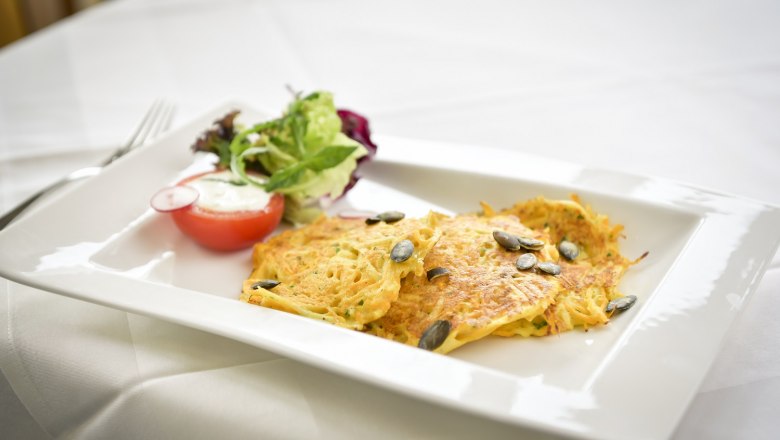 Gesunder Genuss, © Moorheilbad Harbach Ein Teller mit Kartoffelpuffer, Kürbiskernen und Salat auf einem weißen Tisch.