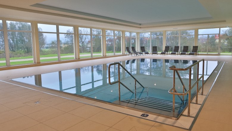 Hallenbad, © Lebens.Med Zentrum Bad Erlach Innenansicht eines Hallenbads mit großen Fenstern und Liegestühlen am Beckenrand.