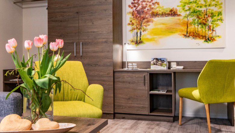 Paket Carpe diem Appartement, © Vitalzeit Hotel Weber Gemütliches Zimmer mit grünen Sesseln, Tulpen auf dem Tisch und einem Landschaftsbild an der Wand.