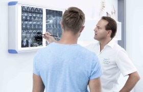 Ein Arzt bespricht mit einem Patienten Röntgenbilder an einer Leuchtbox.