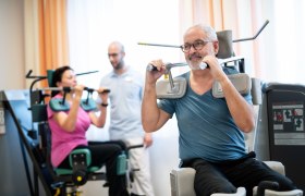 Zwei Personen trainieren an Fitnessgeräten, während ein Trainer zuschaut.