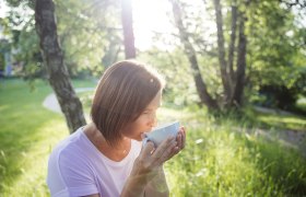 Frau trinkt Tee im Freien bei Sonnenschein.
