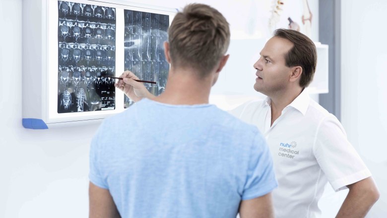 Ein Arzt bespricht mit einem Patienten Röntgenbilder an einer Leuchtbox.