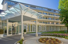 Moderner Gebäudeeingang mit Glasdach und Garten.