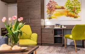 Gemütliches Zimmer mit grünen Sesseln, Tulpen auf dem Tisch und einem Landschaftsbild an der Wand.