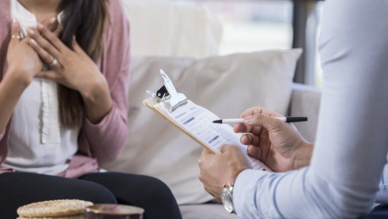 Zwei Personen in einem Gespräch, eine Person hält ein Klemmbrett mit Formular.