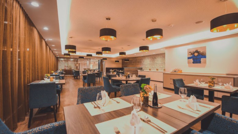 Elegantes Restaurant mit gedeckten Tischen, blauen Stühlen und moderner Beleuchtung.
