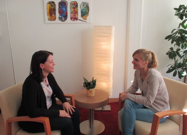 Zwei Frauen sitzen sich in einem gemütlichen Raum gegenüber und unterhalten sich.