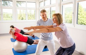 Personen machen Fitness&uuml;bungen in einem hellen Raum mit Fenstern.