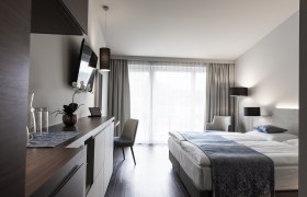 Modernes Hotelzimmer mit Doppelbett, Fernseher, Schreibtisch und Balkon.