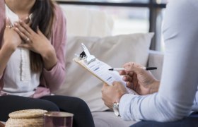 Zwei Personen in einem Gespräch, eine Person hält ein Klemmbrett mit Formular.